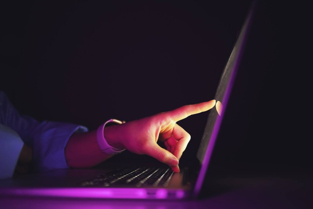 Against a dark background, a closeup of a hand touching a laptop screen.